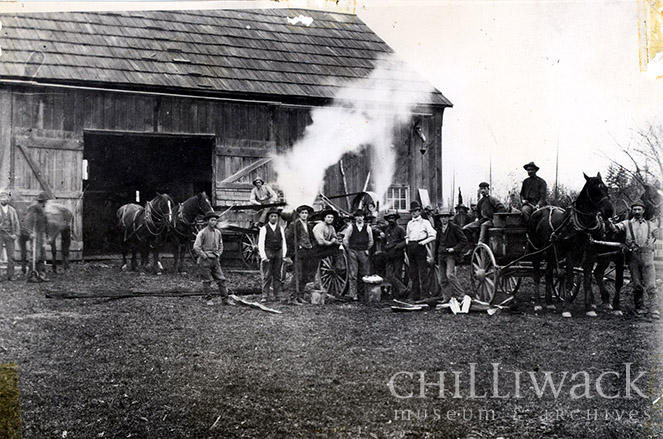 Groupe d’hommes près d’une batteuse à vapeur Kipp & Nowell devant la grange Nowell 