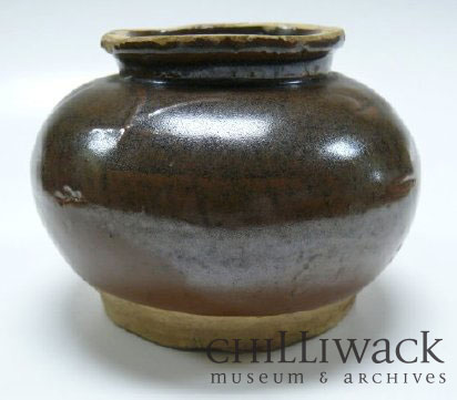 Round dark brown glazed ceramic jar with lipped opening. Chinese characters on the side of jar.