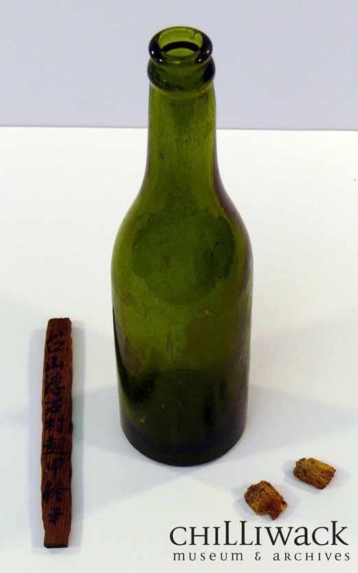 Green glass bottle with a crown top and two pieces of cork. Wooden marker inside bottle shows Chinese characters on both sides.