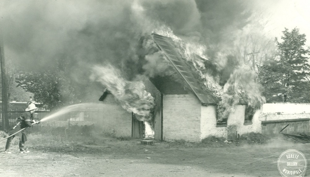 Picture of a fire engulfing a small building, there's also a fire fighter spraying water on to the building.