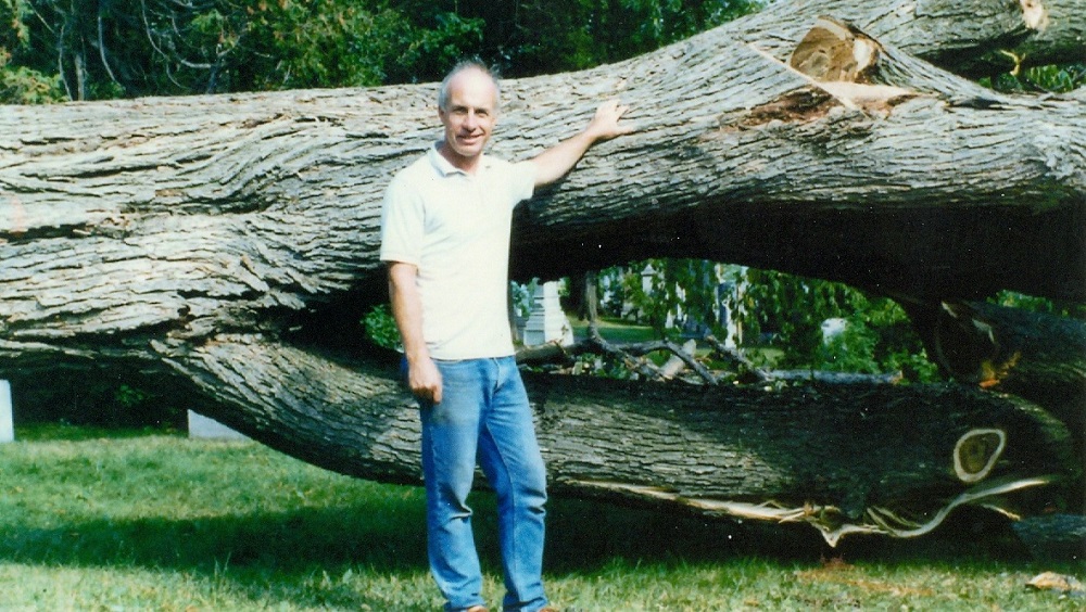 Colour picture of a man leaning on a massive tree trunk that was cut down