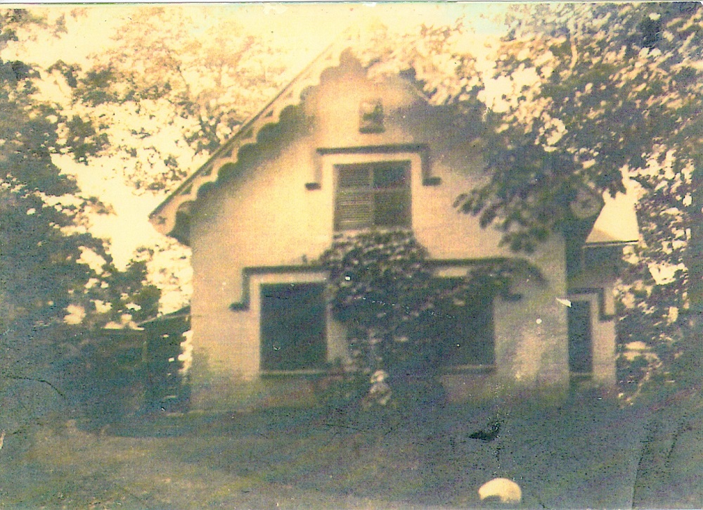 Gray and white picture of a white house with English colonial details surrounded by trees.