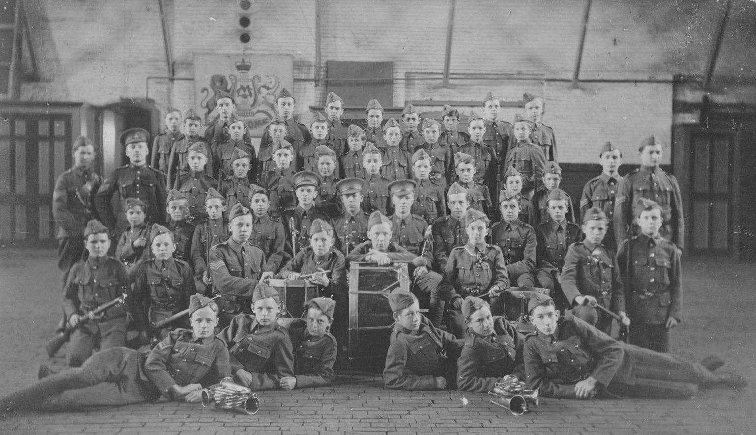 black and white photo of a group of boys dressed in a military uniform standing in a gymnasium.