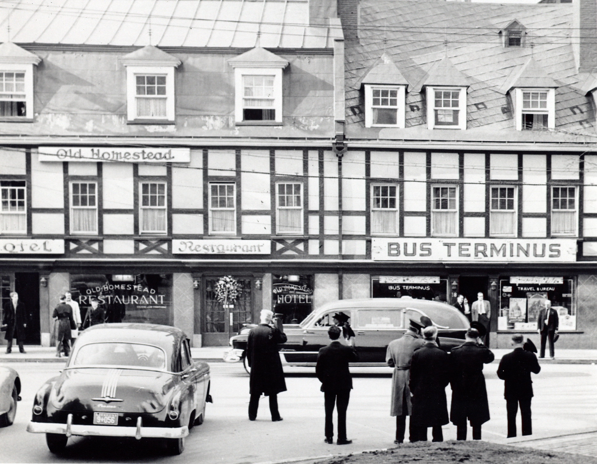 Black and white picture of a funeral procession, many black cars are driving down a road.