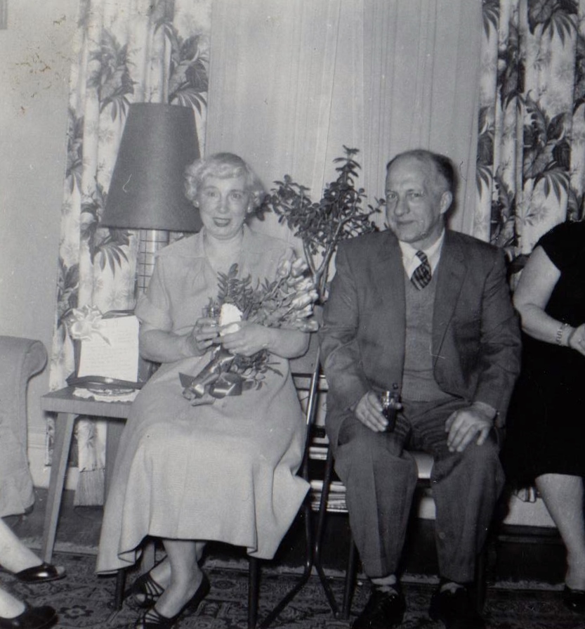 Black and white picture of an older couple at a party dressed in their best sitting by a large window