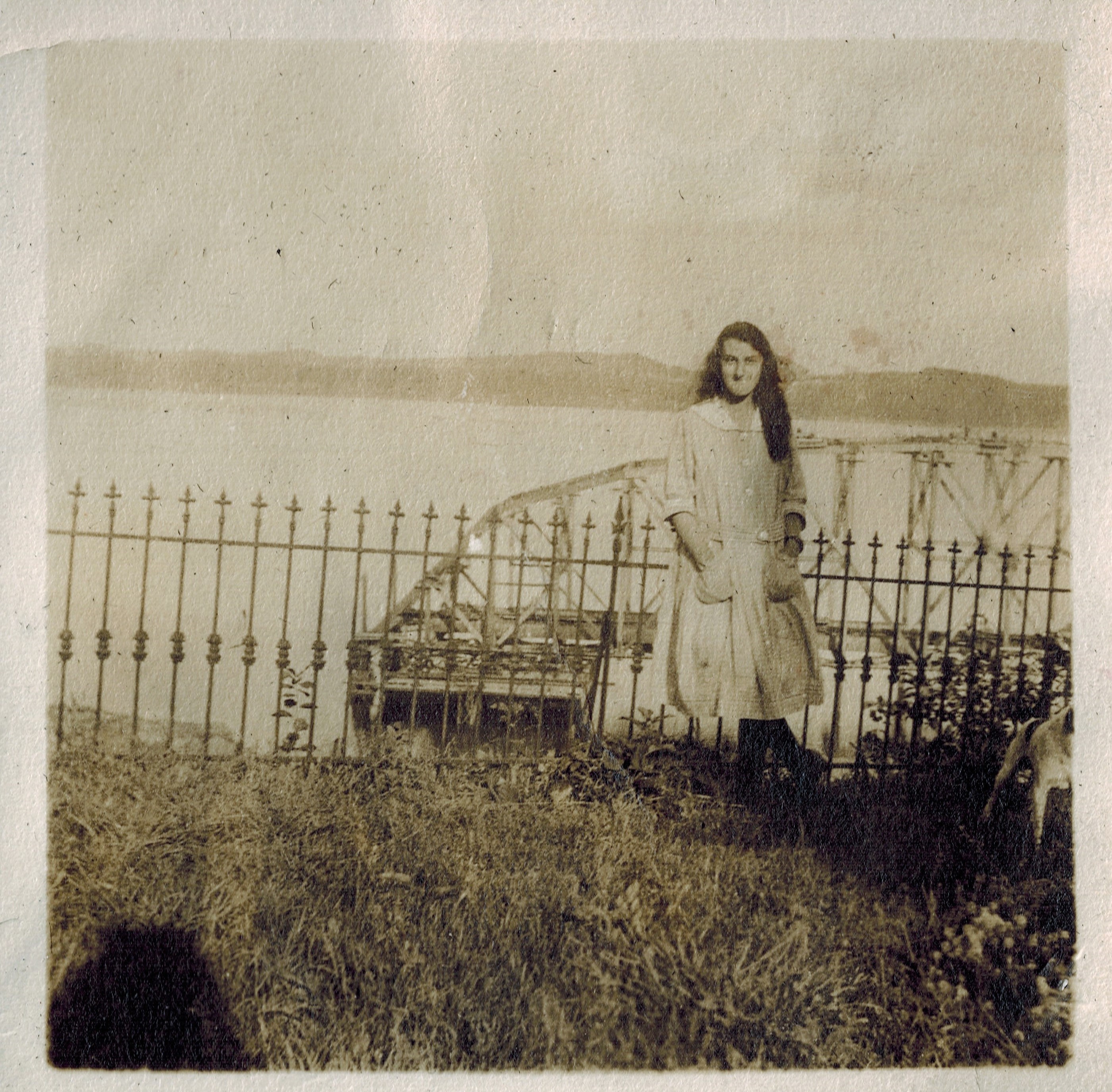 sepia photo of a girl dressed in a white dress in front of a bridge