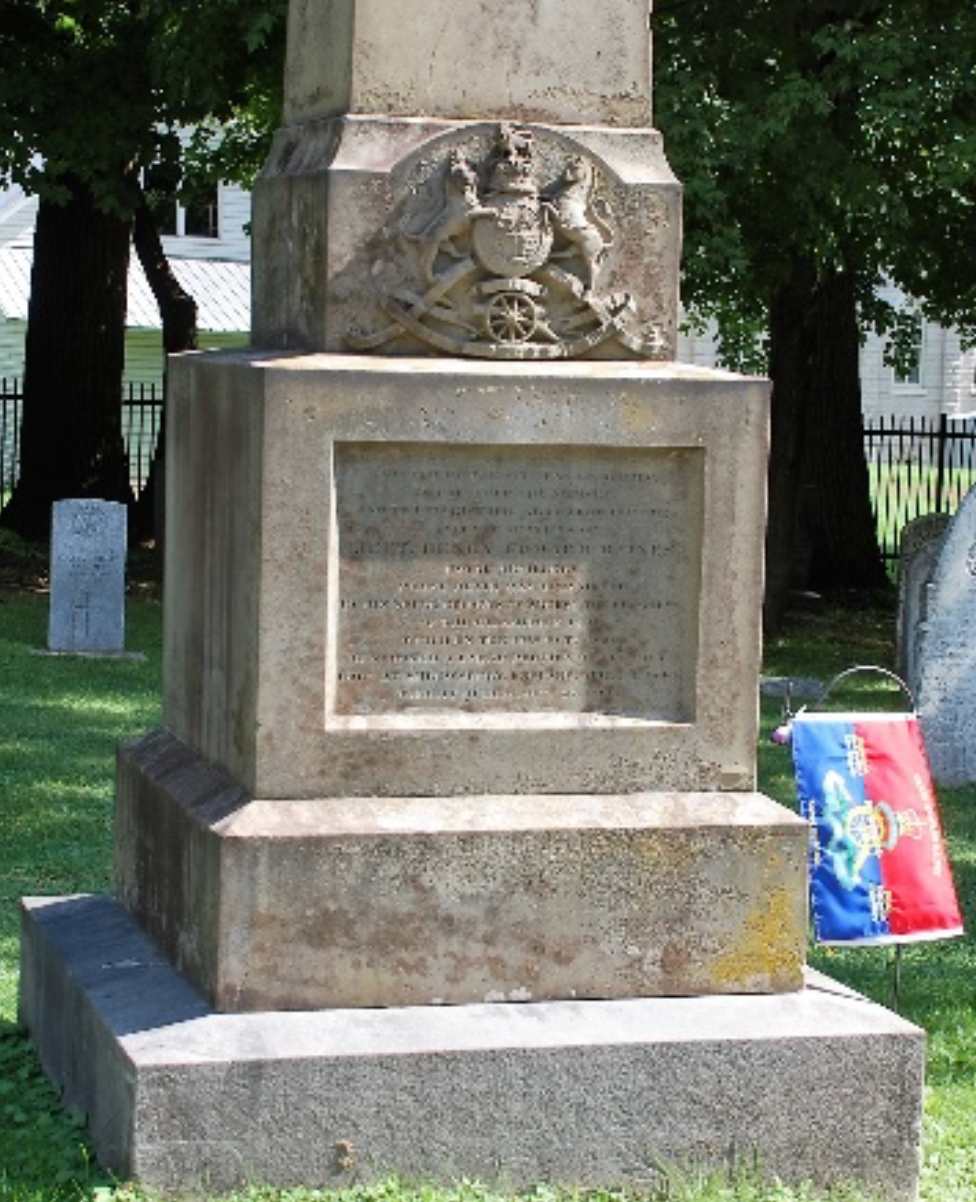 Grey Headstone in the trees with a red and blue flag