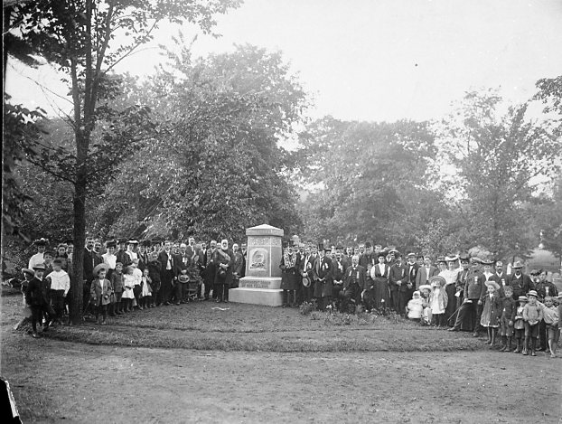 Black and white picture of a large group of people surrounding a cemetery monument for a picture