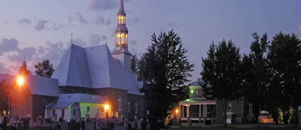 Color photograph, long shot taken at night, back view of church, presbytery and cemetery, the exterior lights of the church are lit.