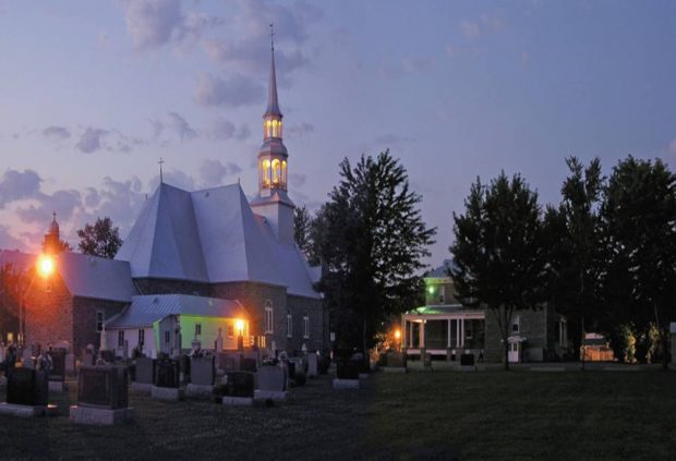 Color photograph, long shot taken at night, back view of church, presbytery and cemetery, the exterior lights of the church are lit.