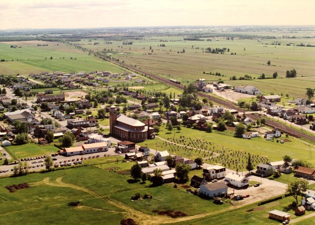 Color photograph, aerial view of a village with a church in the center, the village is surrounded by farm land.
