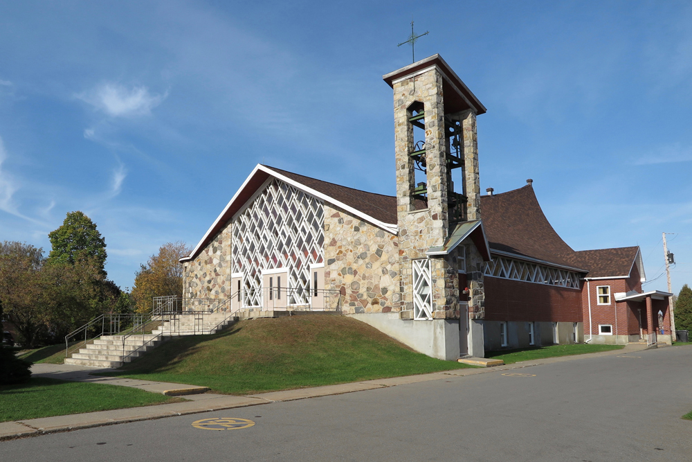 Color photograph, long shot of a stone and brick church with an atrium in the façade, on the building’s right, a square stone steeple that is open on all four sides.