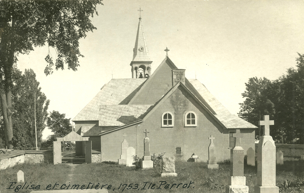 Old black and white photograph, long shot of a cemetery surrounded by a low wall and trees, located behind a multiple-sloped roof church and steeple.