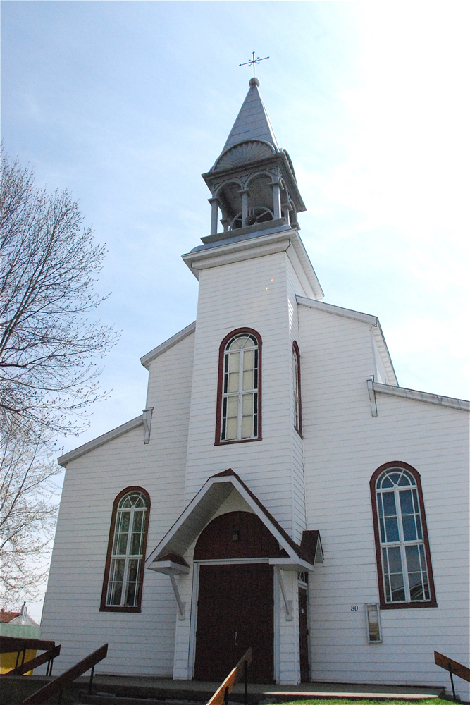 Color photograph, close-up of a white wood church facade with a steeple and front porch.