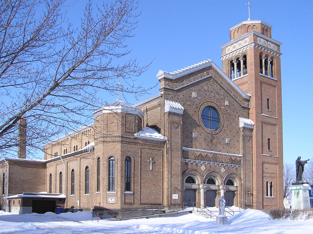 Color photograph taken in winter, long shot of a large brick church with an imposing steeple on the building’s righthand side.