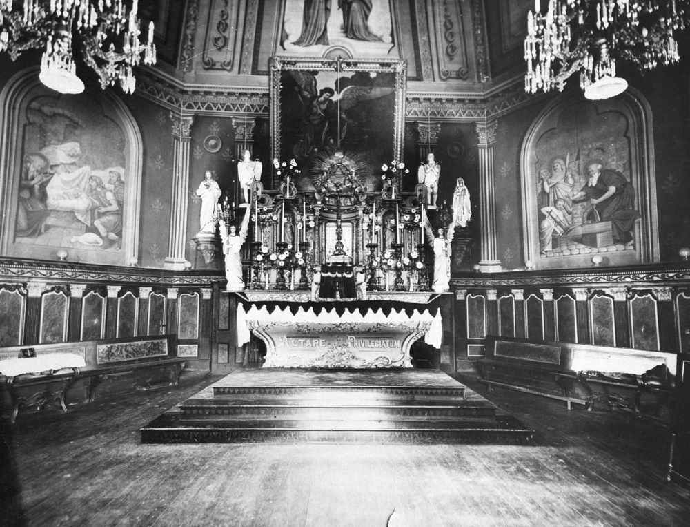 Old black and white photograph, long shot of richly decorated church interior and liturgical furnishings, statues and religious paintings.