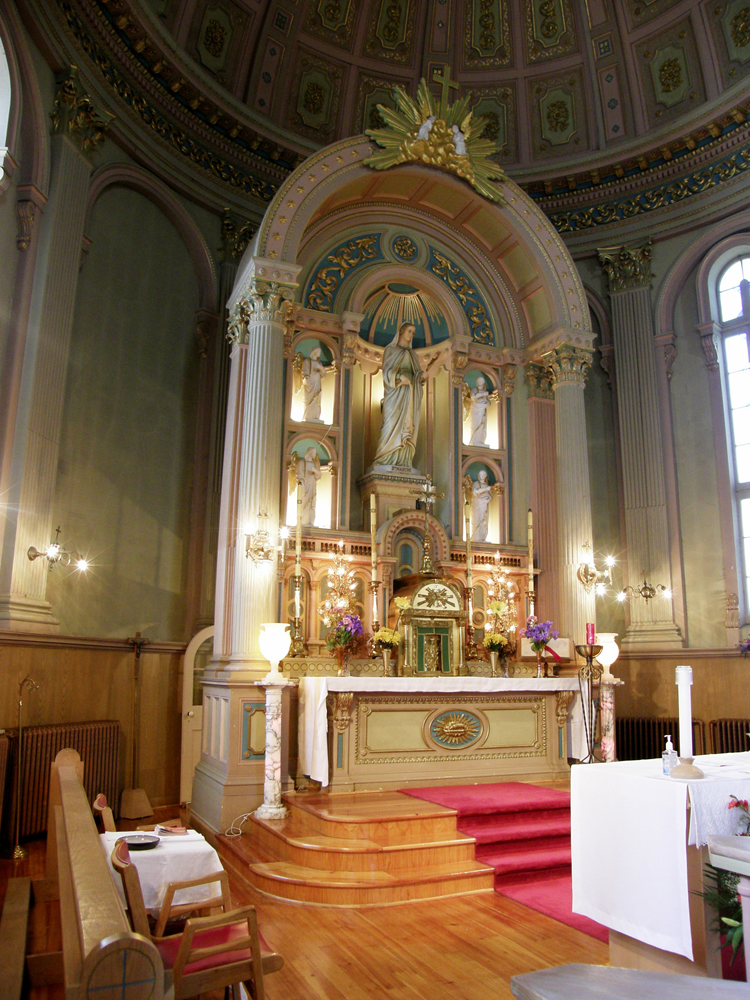 Color photograph, close-up of a church interior with religious furnishings on which stands a large statue surrounded by four smaller lighted statues.