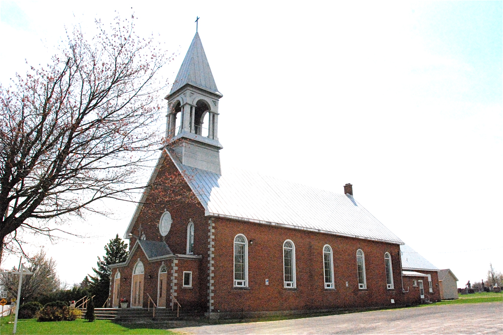 Color photograph, long shot, side-view of a red brick church with an angled roof and metal steeple.