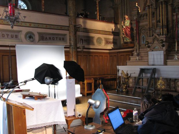 Color photography, close-up of church containing photographic material, various religious objects on tables and a woman working at a computer.