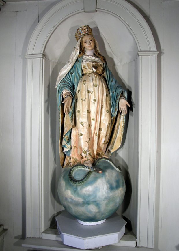 Color photograph, close-up of a gold and blue statue representing a woman wearing a crown and standing on a globe, arms outstretched, she is crushing a snake at her feet.