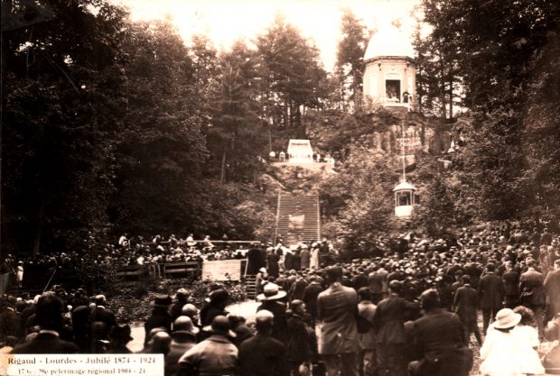 Old black and white photograph, a crowd is assembled at the foot of a large hill, a large staircase leads to a rotunda that is surrounded by trees.