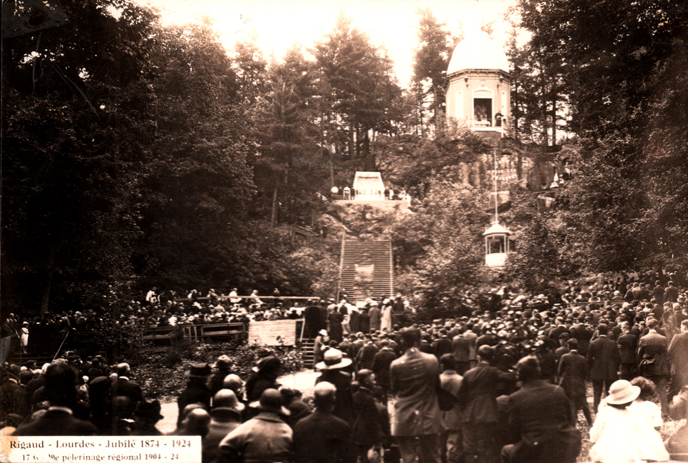 Old black and white photograph, a crowd is assembled at the foot of a large hill, a large staircase leads to a rotunda that is surrounded by trees.