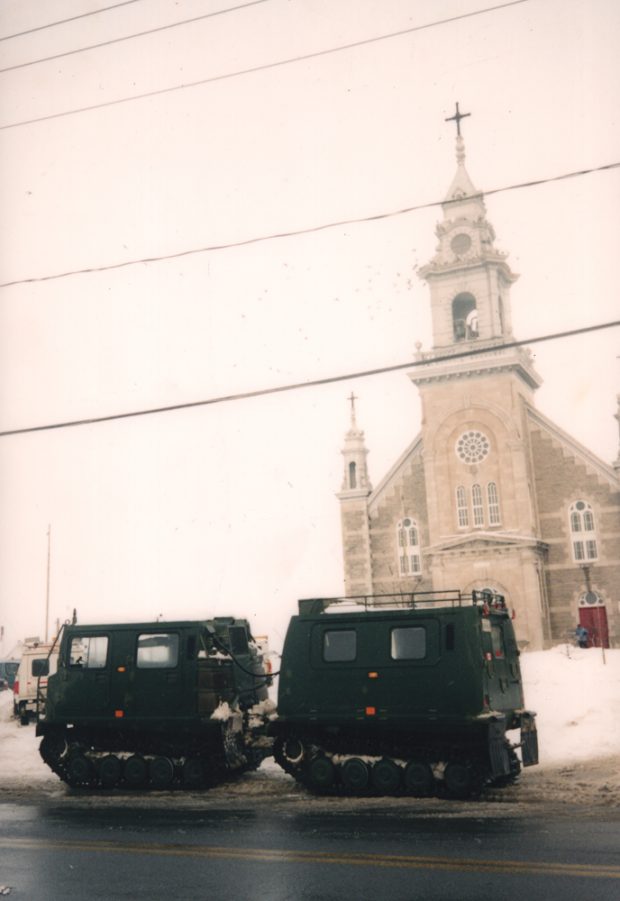 Color photograph taken in winter, long shot, two military vehicles are parked near the front door of a large stone church.