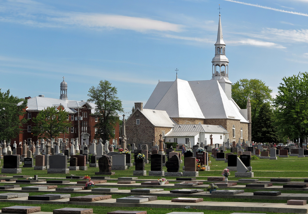 Color photograph, long show, in the foreground, a large cemetery, in the background, a stone church and its steeple. To the left of the building, a large red brick structure topped with a dome.