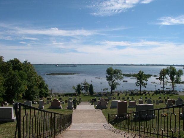 Color photograph, long shot, in the foreground a long staircase descends through a cemetery towards a large river in the background.