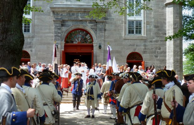 Color photography, long shot of a crowd wearing various period costumes on the front steps of a stone church after Sunday Mass.