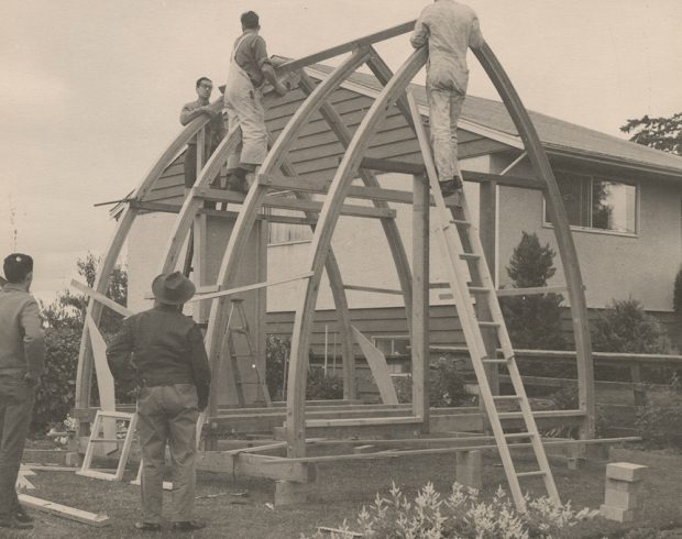 BCMC members work on assembling the Hut in the front yard of a club member and two others stand watching the construction process.