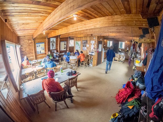 Groups of people sit at tables in the wide-open main room and the cooking area is tucked in the back right corner.