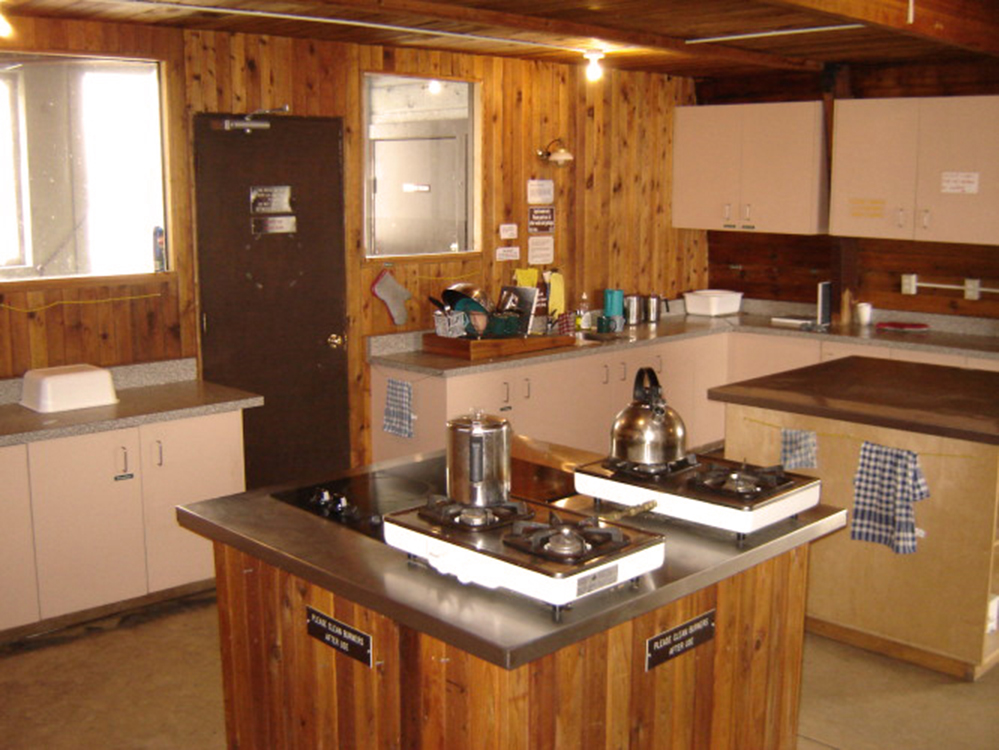 4 gas burners sit on one island countertop next to two additional burners. Another island is free for prep space and cupboards and countertops are located in the background against the wall.