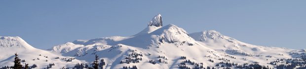 The volcanic black tip of the Black Tusk dusted with snow stands above the other peaks buried in a deep layer of snow.