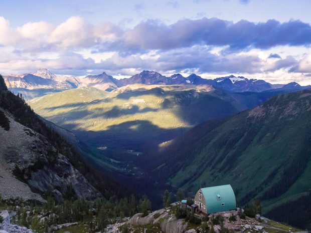 Photo was taken from above the Conrad Kain Hut and looks out across the lush green valley to bare glaciated peaks on the other side. The storm clouds display shadows on the sunny side of the valley.