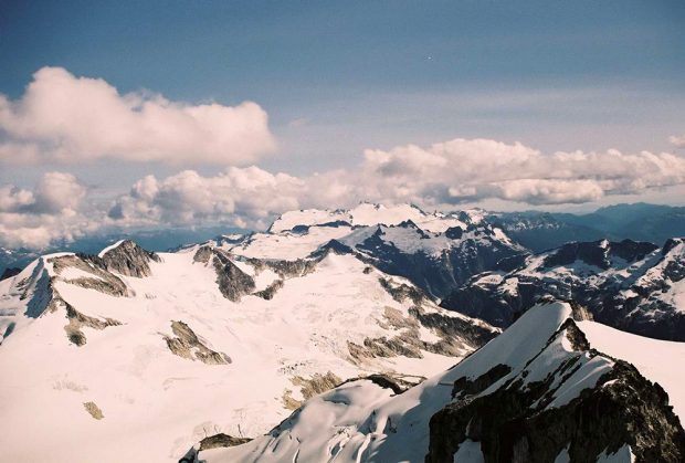 Isoscoles and Mamquam Mountains covered with large puffy clouds hanging above the peaks in the summer sunshine.