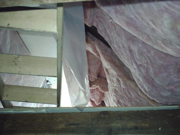 Pink insulation hangs from the roof of the Hut and plastic sheeting is attached on one side but not the other. An empty wooden ladder rests against a wooden beam.