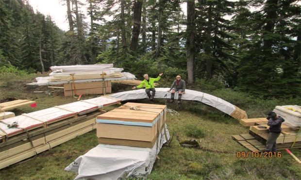 Loads of lumber and supplies for building the hut dropped off by helicopter at the remote worksite. Club members pose in different positions on or near the supply loads.