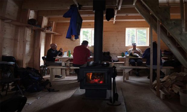 The orange flames and embers can be seen burning inside the dark black stove. A group of the construction crew sits at a long table enjoying a break.