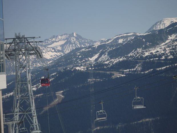 A red gondola car descends from a large steel tower on Whistler Mountain and across the valley is the peak of Blackcomb Mountain and the Armchair Glacier.