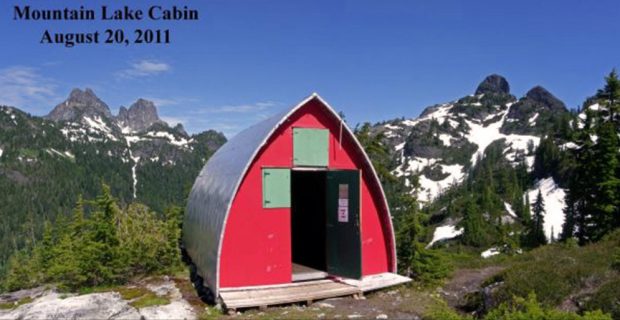 The Mountain Lake Hut front door stands ajar with the pale green window shutters closed and the front end wall now painted a bright red.