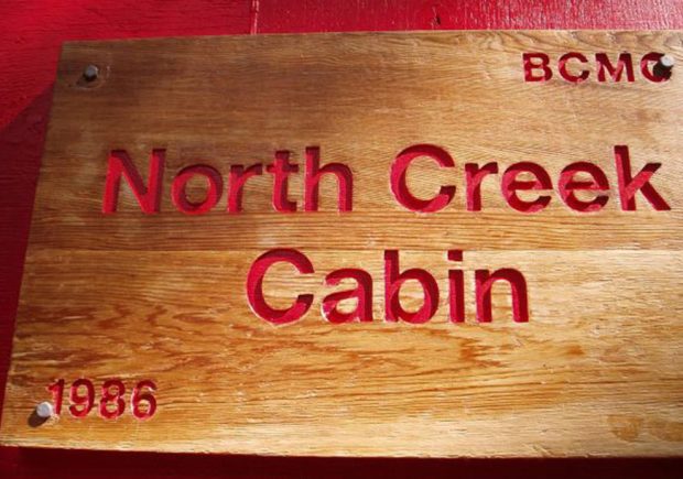 Close-up of the freshly stained and painted sign for the North Creek Cabin mounted next to the front entrance.