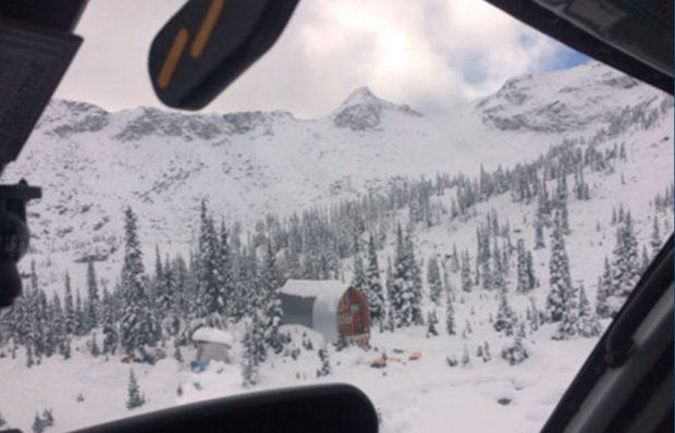 Aerial view of the Hut from a helicopter window and snow covers the ground, evergreen trees and high peaks behind the Hut.