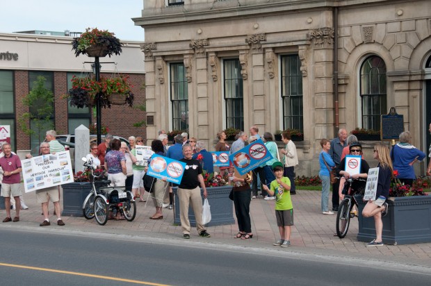 colour photograh of small crowd of adults and children waving placards on sidewalk in front of building