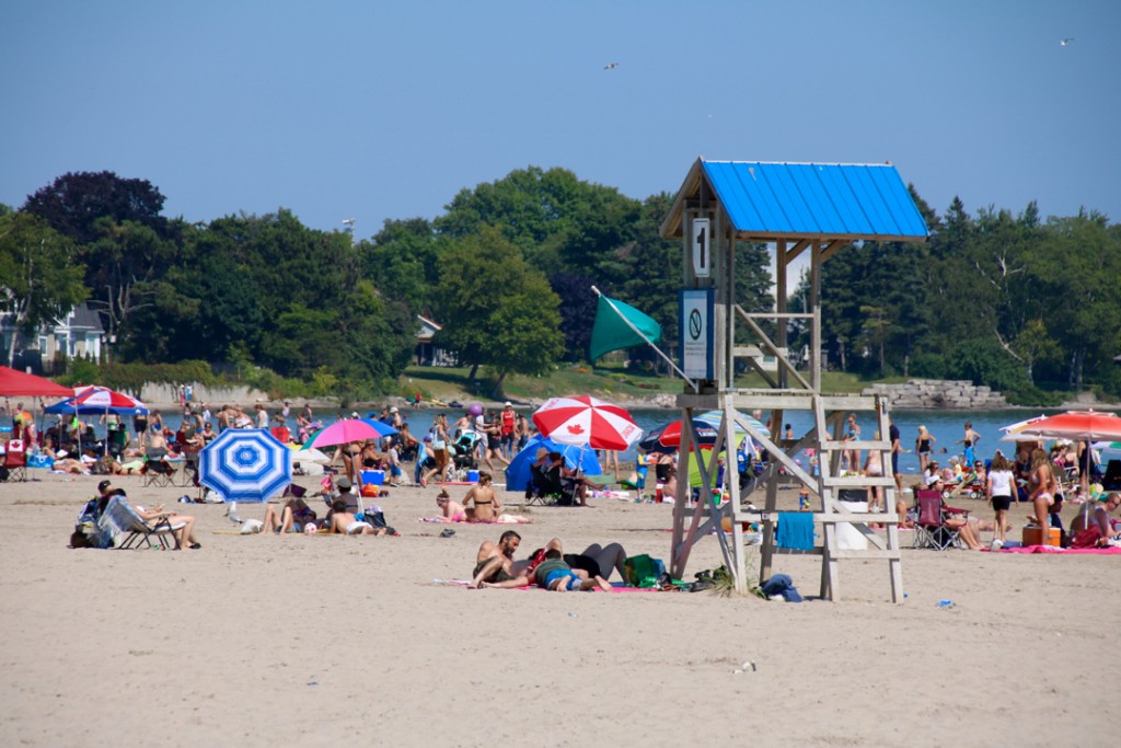 colour photograph of people lying on sandy beach with colourful umbrellas, life guard station unmanned