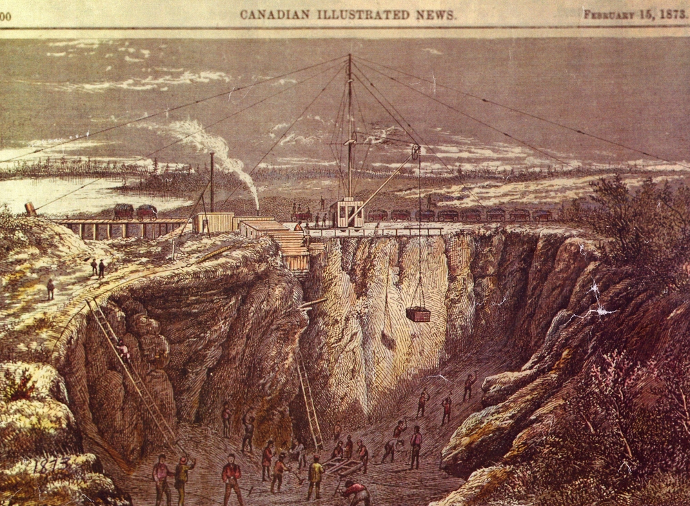 a coloured etching from the Canadian Illustrated News dated February 15, 1873 with at least 20 men performing various tasks in a deep open faced mine. At the top of the mine and the centre of the etching is a large derrick help in place by multiple guy wires. Behind the derrick is a row of railway cars