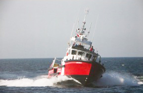 a colour photograph of a red and white vessel in open water heading toward the camera