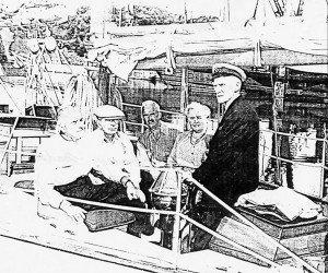 a poor quality photocopy of a photograph of five people in the stern of a boat, four seated and one standing wearing a captain's cap