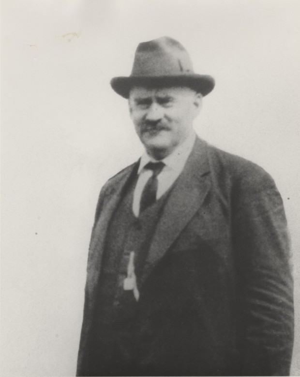 John R. Kerr is staring at the camera. It appears the photograph was taken outdoors. He is wearing a fedora, jacket, vest, shirt and tie.