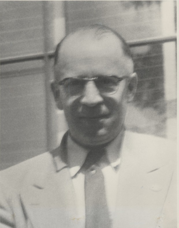 Harry F. Bickford is looking at the camera. He is wearing glasses, a jacket, shirt and tie. It appears the photograph was taken outdoors where Harry may be standing outside of a building.